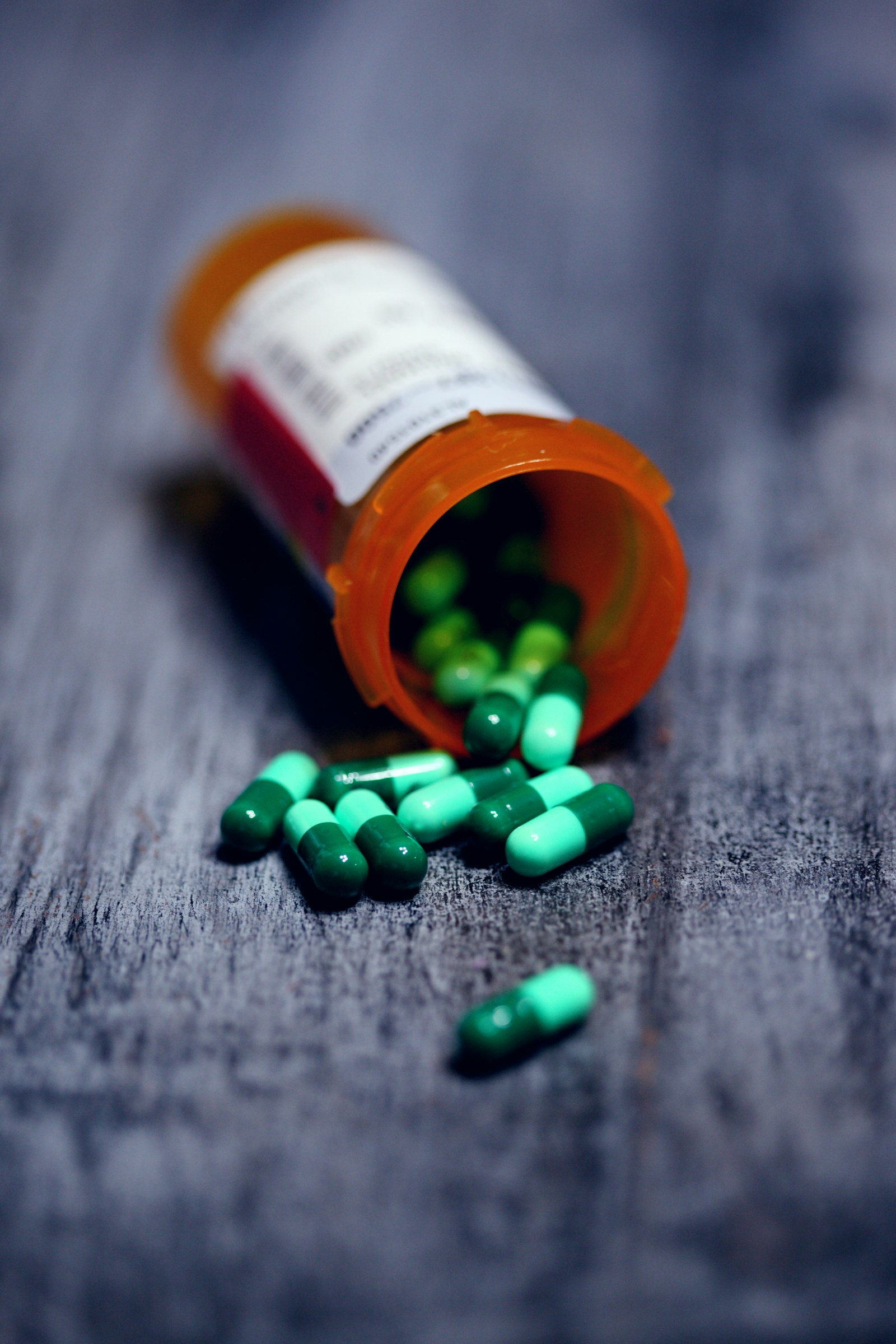 A generic prescription bottle with green capsules on a table